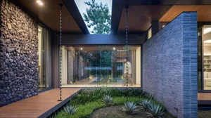 A modern house exterior featuring a wooden deck, stone wall, and greenery.