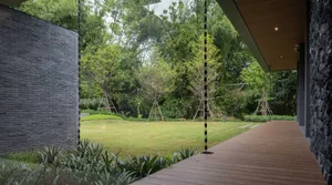 Modern outdoor space featuring a wooden deck, stone walls, and glass elements surrounded by lush greenery.