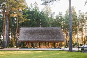 A rustic holiday house with a thatched roof and glass walls.