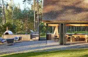 Modern residential exterior featuring a thatched roof, stone patio, wooden deck, and glass doors.