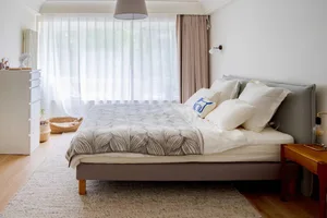 A minimalist bedroom with a bed dressed in white towels with a blue and white pillow.
