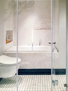 Modern bathroom with white marble walls and floor, white bathtub, and white toilet.
