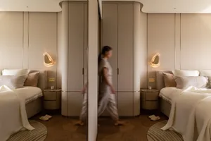 A modern bedroom with neutral-toned walls, flooring, and furnishings, featuring two beds, wall sconces, and a large closet.