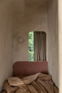 A minimalist bedroom with a pink velvet headboard and a cozy atmosphere, featuring a round light on the wall and a view of gr