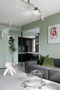 Modern living room featuring a gray sofa with green throw pillows, a green floor lamp, and a green plant in a concrete plante