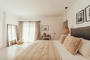 A minimalist bedroom featuring light-colored bedding and woven fabric elements.