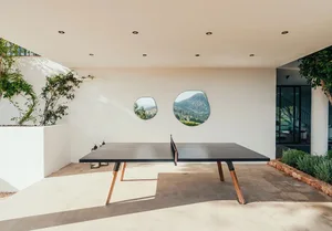 Minimalist patio featuring a concrete ping pong table with a mountainous backdrop through circular windows.