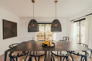 A modern dining room featuring a metal table with hanging rattan pendant lights and chairs with woven seats, set against a wh