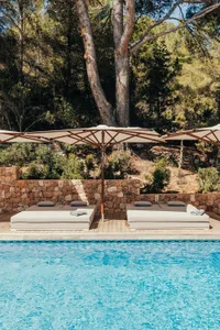 Swimming pool with lounge beds and umbrellas surrounded by trees and a stone wall.