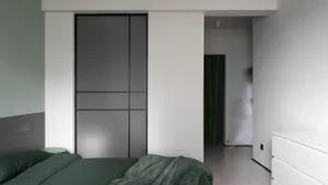 Minimalist bedroom with green bedding, black metal sliding doors, and white walls.
