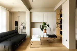 Modern minimalist living room with a black leather sofa, wooden flooring, and white cabinets.