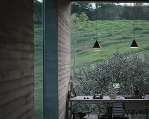 View of a minimalist residential kitchen featuring concrete walls and stainless steel appliances, overlooking a green hillsca