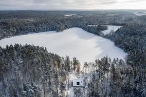 Minimalist-style vacation home nestled among snow-covered trees and a frozen lake.