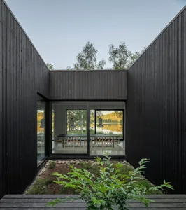 Modern black interior with contrasting elements, glass and wood materials, and a serene outdoor view.