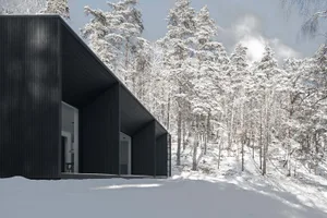 A modern black metal house surrounded by snowy trees.
