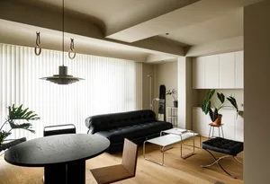 A modern living room with a black sofa, white blinds, and minimalist decor.