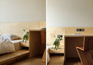 A minimalist bedroom with a wooden platform bed and built-in storage units, featuring a green plant and a desk area.