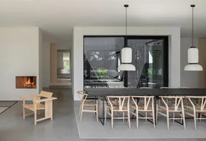 Modern minimalist dining room with wooden chairs, concrete floor, and large black-framed windows.
