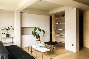 A modern minimalist living room with a black couch, white coffee tables, and wooden flooring.