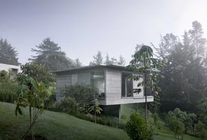 A modern residential home made of concrete with large glass windows overlooking a forested landscape.