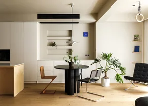 A modern residential kitchen with hardwood flooring, featuring sleek black appliances and a round dining table with green pla