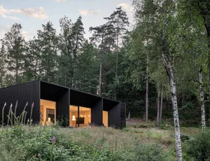 A modern residential building with wooden exterior surrounded by trees and flowers.