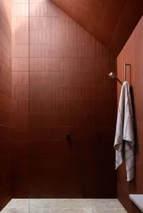 Modern minimalist bathroom with terracotta tiles, featuring a sleek shower area with a handheld showerhead and a towel hangin