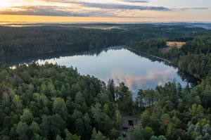 A serene landscape featuring a tranquil lake surrounded by dense forests at sunset.