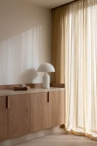 A modern minimalist interior design featuring a wooden cabinet with a white table lamp and a clear glass vase.
