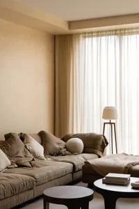 A minimalist living room with a fabric couch, wood coffee table, and white curtains.