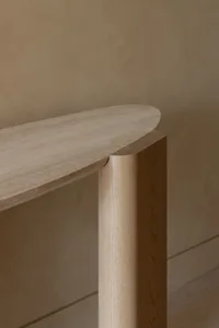 A minimalist wooden console table with curved edges, placed against a beige wall.