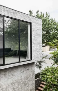 Modern gray brick exterior with large windows reflecting greenery and trees.