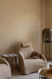 A modern, minimalist living room with a beige fabric armchair, a side table with a marble top, and a floor lamp with a transp