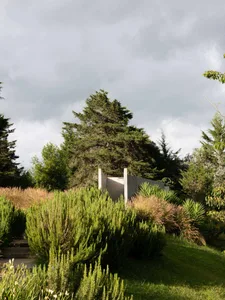 A modern landscape featuring a concrete structure surrounded by greenery and trees under a cloudy sky.