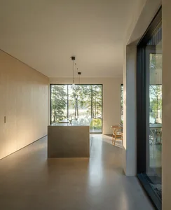A modern residential kitchen featuring a concrete floor and island, with large windows showcasing a serene outdoor landscape.