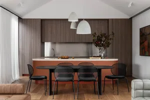 A modern residential kitchen with wood cabinets, a stainless steel backsplash, and a black dining table with black chairs.