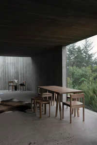 A modern interior with wooden furniture, concrete walls, and glass windows, featuring a table and chairs.