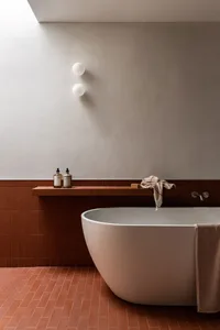 Modern minimalist bathroom featuring terracotta tiles and concrete finishes, with a sleek freestanding bathtub and simple fix