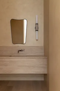 Modern bathroom vanity unit with a stone countertop and sink, featuring a sleek faucet and a large mirror with a wavy frame.