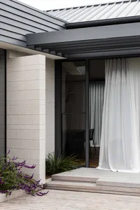 A modern house entryway with a concrete column and wooden deck, featuring sheer curtains.