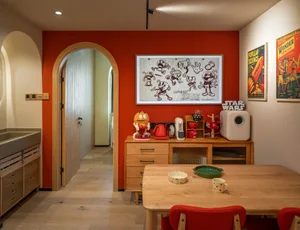 A modern kitchen interior with a red accent wall, wooden table, and various decorative items.