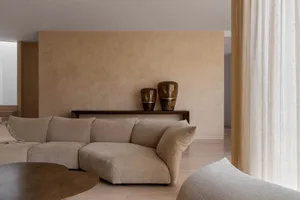 A modern living room with a neutral-toned sofa, minimalist decor, and large windows.