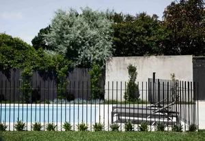Modern minimalistic swimming pool enclosed by a concrete fence with landscaping and concrete seating.