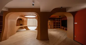A modern living room with curved wood paneling, wooden floors, and red accents.