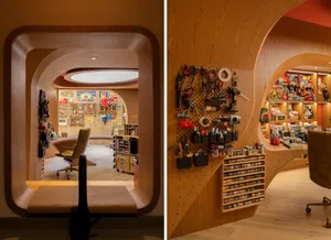 A modern workspace with curved wooden walls, an array of tools and supplies, and various books and toys on shelves.