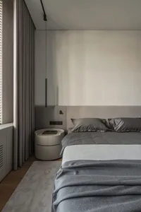Modern, minimalist bedroom featuring a gray upholstered bed, glass nightstand, and dark wood flooring.