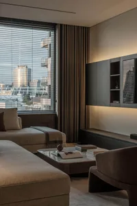 Modern living room with neutral-toned furniture, minimalistic design, and cityscape view through large windows.