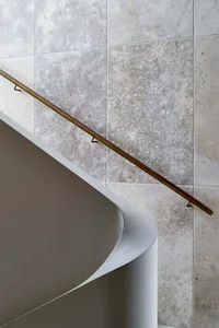 A modern staircase featuring a bronze metal railing against a textured wall.