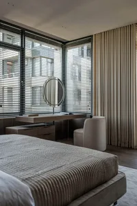 A modern bedroom featuring a large bed with a fabric headboard and a sleek, minimalist desk with a round mirror in front of a
