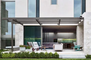 Modern concrete patio featuring a pergola, plants, and outdoor furniture under a shaded area.